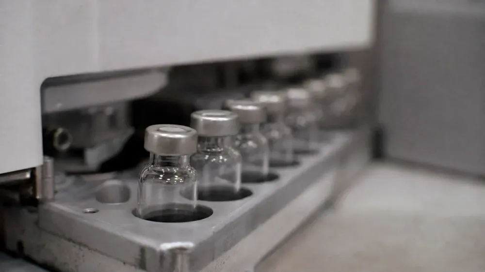 A row of small clear glass vials standing in a metal autosampler tray on a laboratory instrument, photographed close up with the background out of focus.