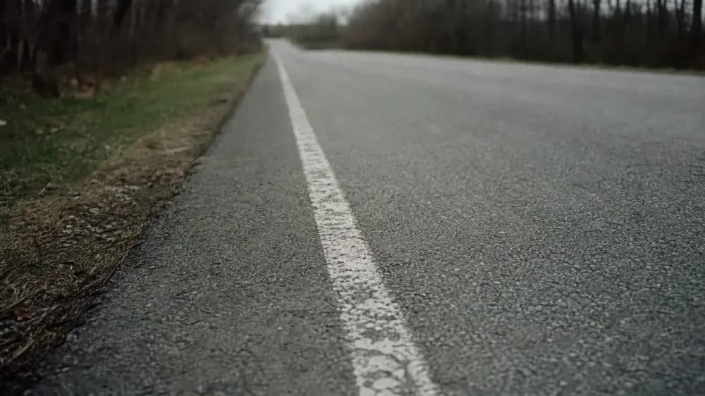 A worn white lane line on grey asphalt, photographed from the roadside of an empty road, the paint scuffed and uneven along one edge.