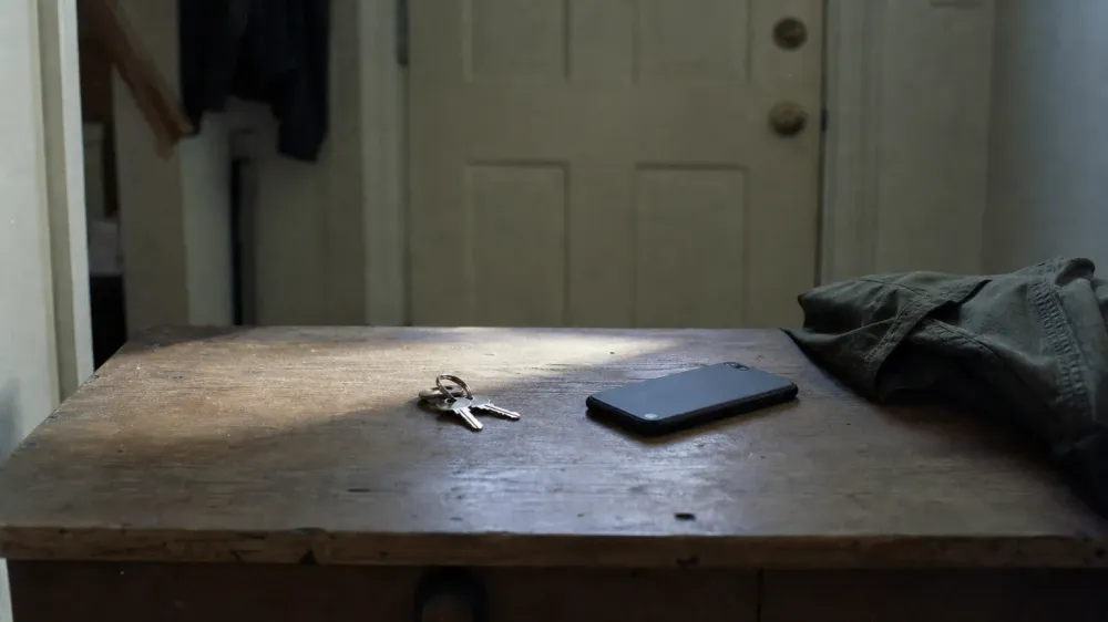 A set of car keys and a phone lying on a worn wooden hall table beside a front door in flat early morning light.