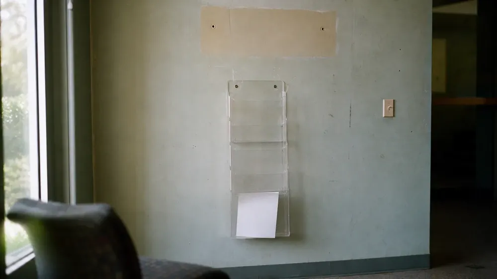 An empty wall-mounted document rack in a public building lobby, every pocket bare except one holding a single blank sheet.