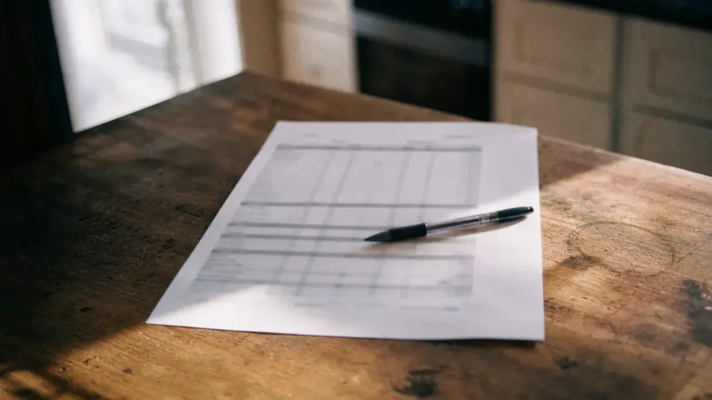 A printed certificate of analysis lying on a kitchen table in morning light, a pen resting across the rows, the type deliberately out of focus and unreadable.