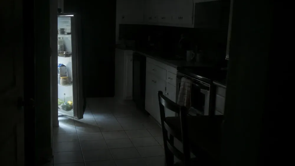 A dark home kitchen at night lit only by the open refrigerator, with nobody in the frame.